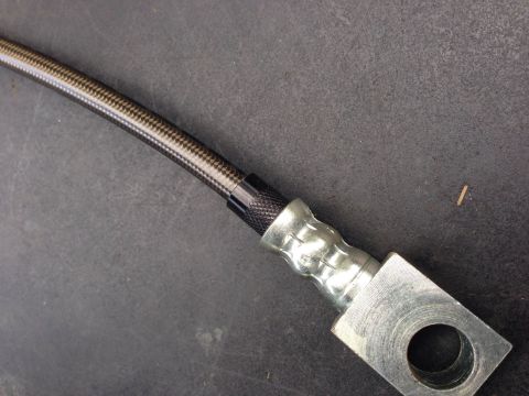 1979 Ford Bronco - A braided brake hose with metal fittings is shown against a dark, textured background.