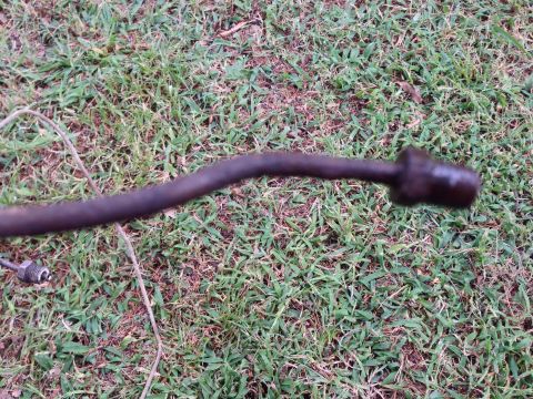 1979 Ford Bronco - A metal rod with fittings, possibly a linkage or hose, rests on a grassy surface.