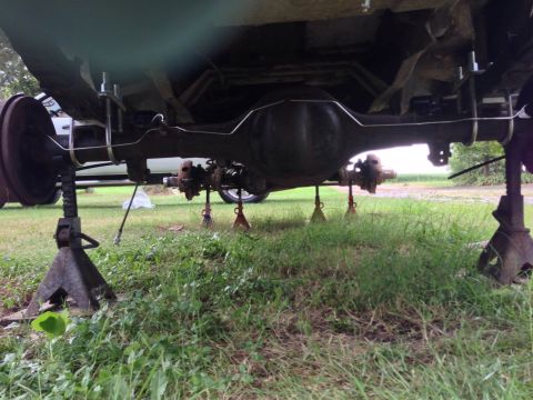 1979 Ford Bronco - The rear axle assembly of a vehicle is elevated on jack stands, revealing the differential, brake drums, and suspension components.