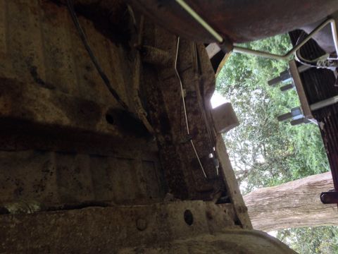 1979 Ford Bronco - Underside view of heavily rusted vehicle frame and suspension components, with greenery in the background.