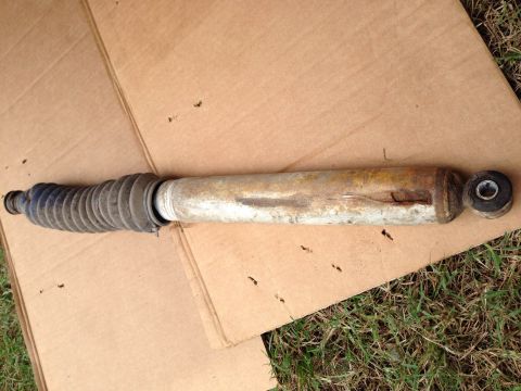1979 Ford Bronco - A single shock absorber with a blue rubber bellows and a corroded metal cylinder is shown on a cardboard surface.