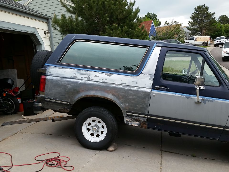 Ford Bronco with primer and rust spots, spare tire on back, parked in driveway