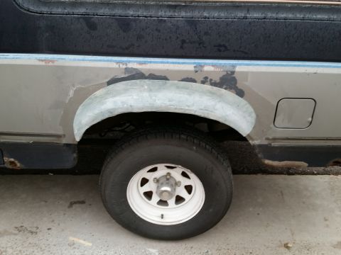 1988 Ford Bronco - Two-tone truck rear quarter panel with gray body filler applied over the rusty wheel arch above a steel wheel.