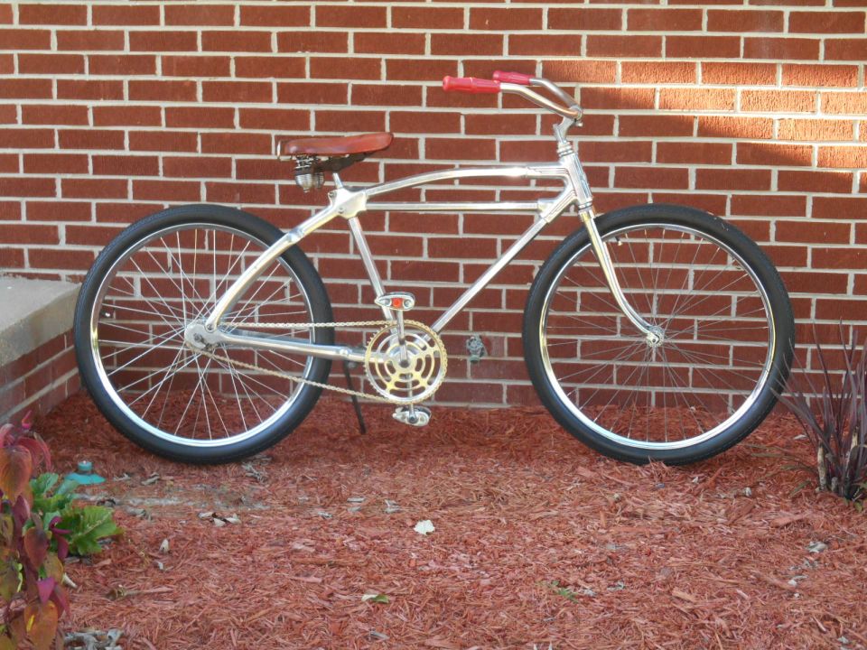 Chrome bicycle with red handlebars and brown seat against brick wall