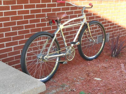 Chrome bicycle with red handlebars and seat, leaning against a brick wall