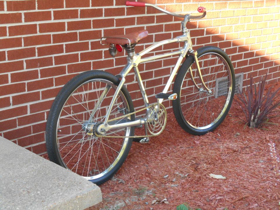 Chrome bicycle with red handlebars and seat, leaning against a brick wall