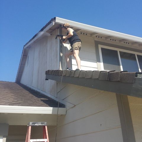 1989 Ford Bronco - A person stands on a roof edge, using a pressure washer to clean the siding of a house.