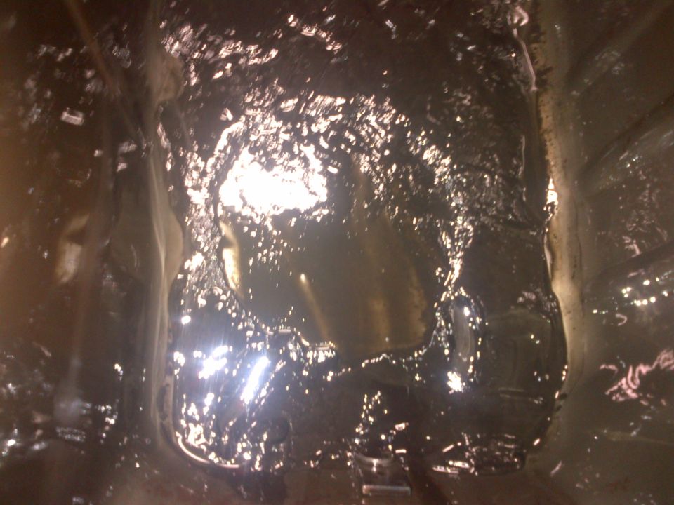 Close-up of a dirty engine oil pan with visible debris and dark oil