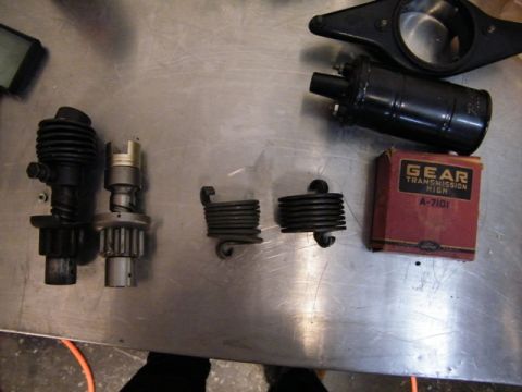 1909 Ford Model T - Several Ford Model T transmission parts are laid out on a metal surface, including a coil and a box labeled 'GEAR TRANSMISSION HIGH'.