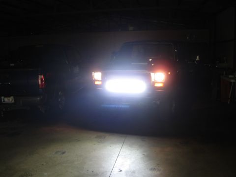 1982 Ford Bronco - A dark garage scene shows two trucks, one with its bright headlights illuminated.