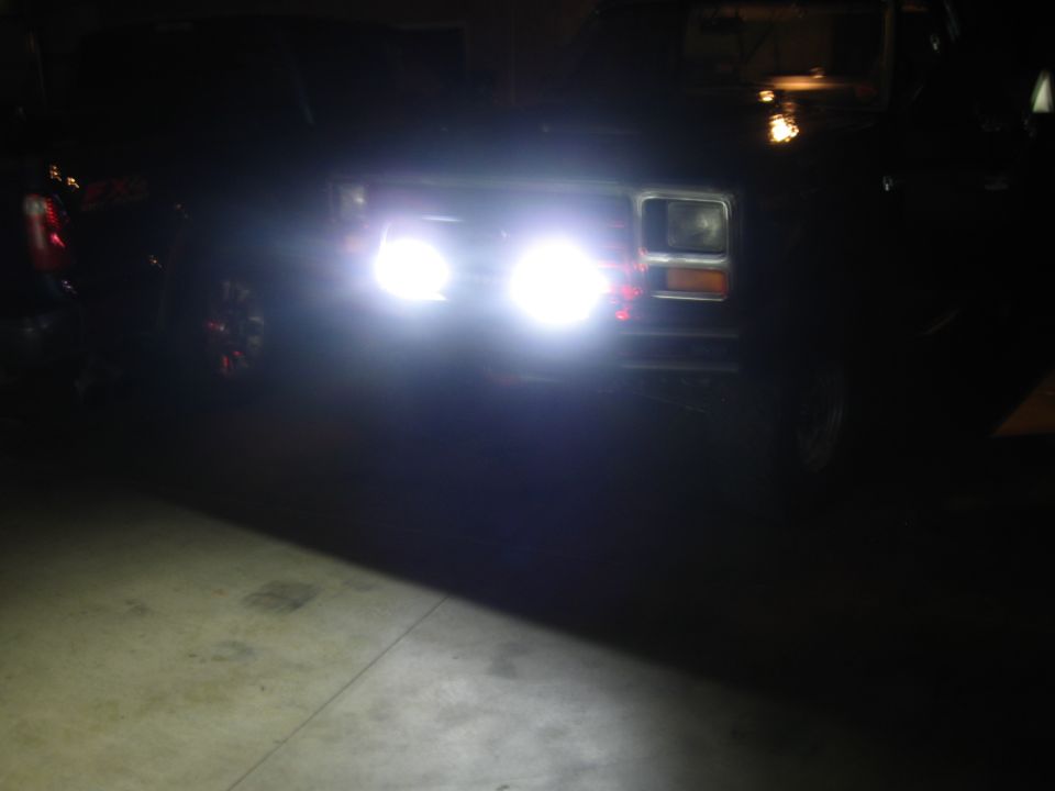 Front view of a dark 1980s Ford Bronco with bright headlights on