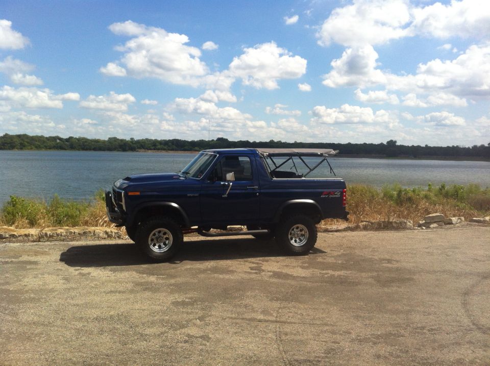 Blue Ford Bronco parked by a lake, side view. Soft top is retracted
