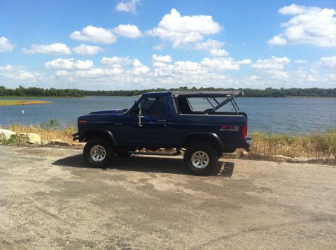1982 Ford Bronco - This 1982 Ford Bronco, with its soft top removed, is parked near a body of water under a cloudy sky.