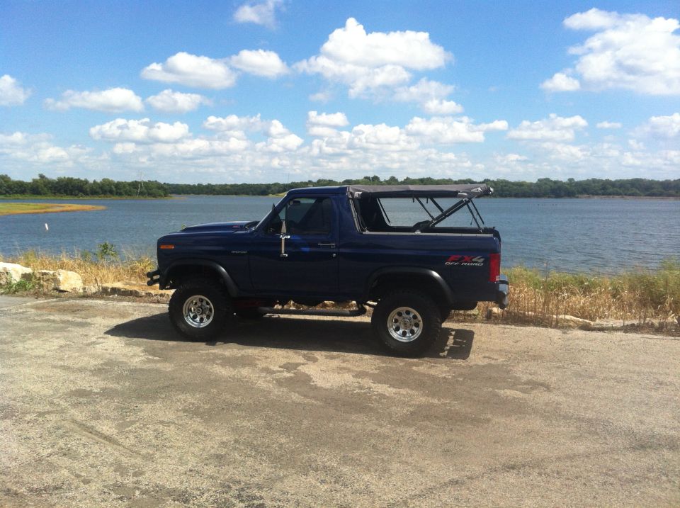 Dark blue 1982 Ford Bronco with soft top removed, parked by a lake