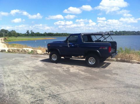 1982 Ford Bronco - This blue Ford Bronco is parked near a body of water on a sunny day with clouds in the sky.