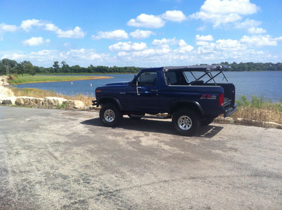 Blue Ford Bronco parked by a lake, top is off