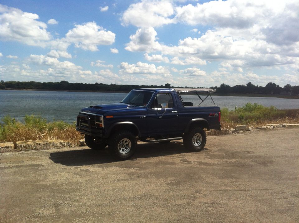 Blue Ford Bronco with aftermarket hood scoop and off-road tires parked by a lake