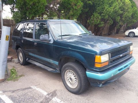 2000 Mercury Grand Marquis - This Ford Explorer SUV is parked in a lot with trees and a fence in the background.