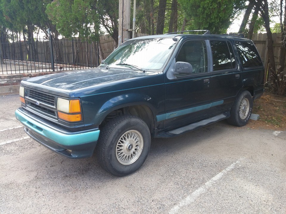 Dark teal Ford Explorer SUV with a light blue lower body trim and front bumper, parked on asphalt
