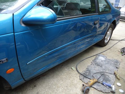 1994 Ford Thunderbird - This blue coupe has significant damage to its driver's side door and fender, with a V8 badge visible.