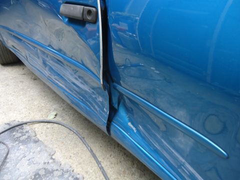 1994 Ford Thunderbird - Close-up of a damaged blue car door and fender, showing denting and misalignment.