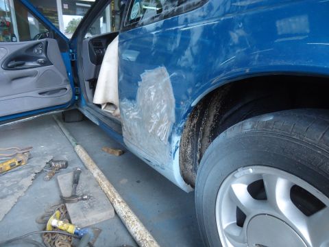 1994 Ford Thunderbird - Bodywork in progress on a blue car, with tools scattered around the work area.
