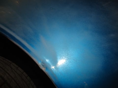 1994 Ford Thunderbird - Close-up of a blue car's fender reveals rust and damage, indicating accident repairs.