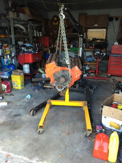 1994 Ford Bronco - An orange V8 engine is suspended by a hoist in a cluttered garage, ready for work.
