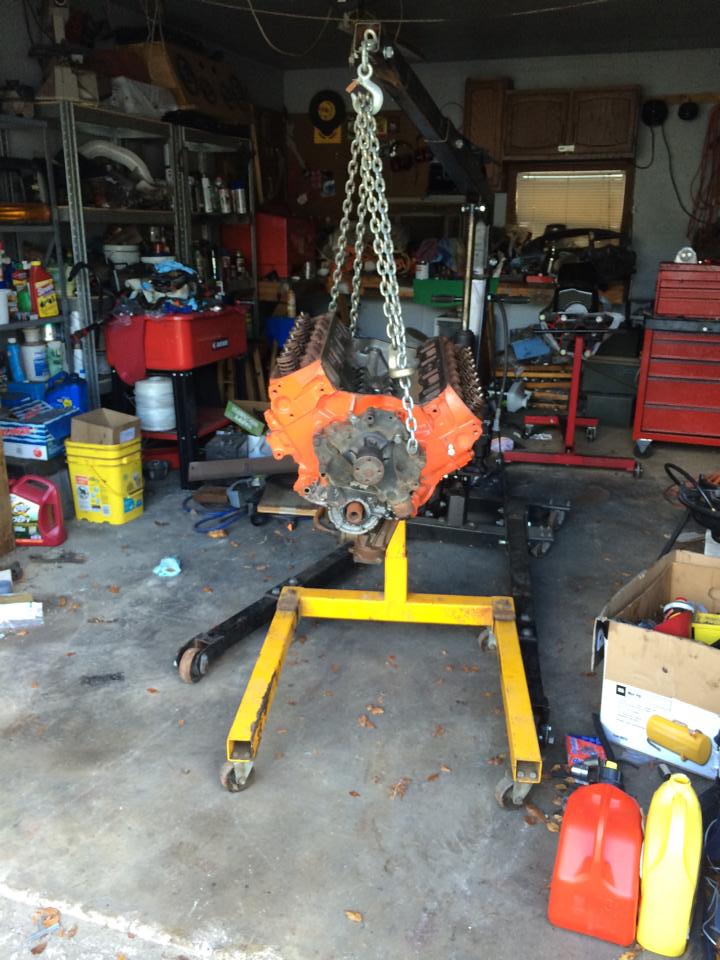V8 engine being lifted by an engine hoist in a garage. It's orange and on a yellow stand