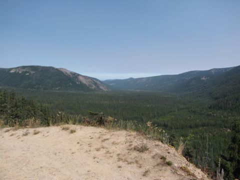 1992 Ford F-150 - A vast, tree-covered mountain valley stretches out under a clear blue sky, with a dirt embankment in the foreground.