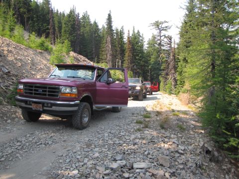 1992 Ford F-150 - A purple 1992 Ford F-150 leads a line of vehicles on a wooded gravel road.