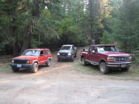1992 Ford F-150 - Three trucks and SUVs parked on a dirt road in a forest setting.