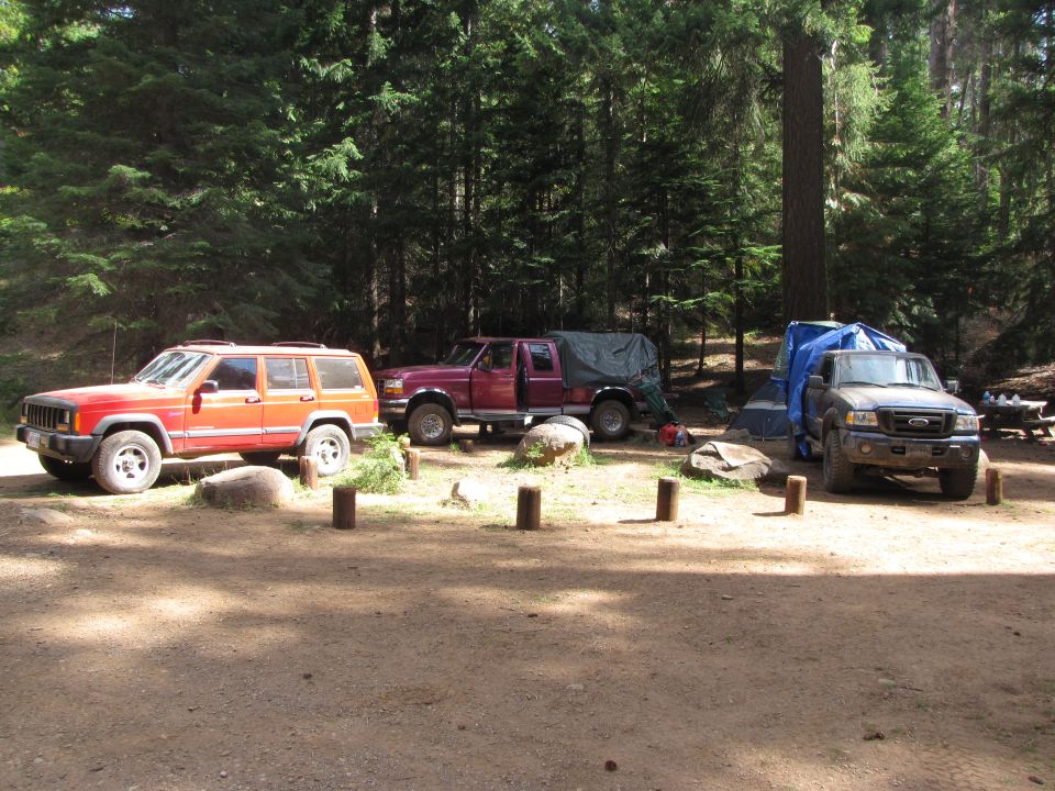 Three trucks and a Jeep parked at a campsite in a forest