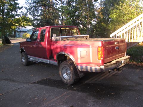 1992 Ford F-150 - A red 1992 Ford F-150 pickup truck is parked on a driveway with trees and a house in the background.