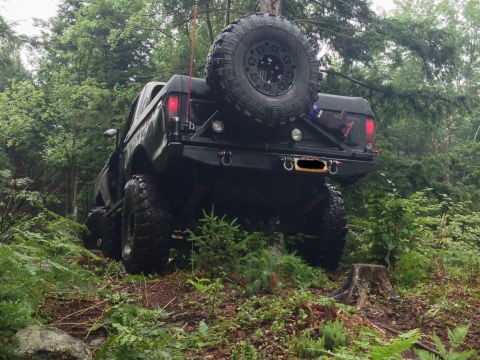1979 Ford Bronco - This modified SUV is navigating a challenging off-road path through a dense forest.