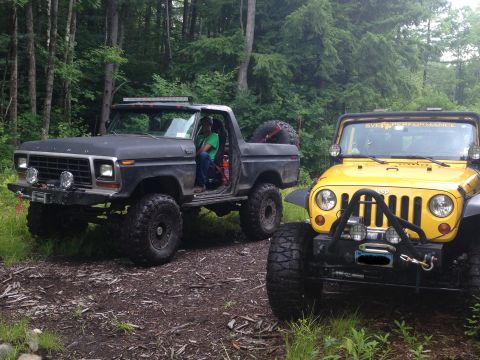 1979 Ford Bronco - Two off-road vehicles, a black 1979 Ford Bronco and a yellow Jeep, are parked on a wooded trail.