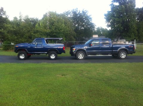 1982 Ford Bronco - A lifted blue Bronco and a blue crew cab pickup truck are parked on a paved driveway.