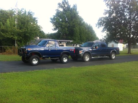 1982 Ford Bronco - Two blue Ford trucks, an older Bronco and a newer F-Series, are parked next to each other on a sunny day.