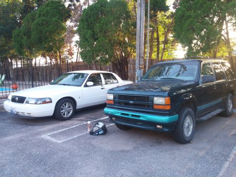 2000 Mercury Grand Marquis - Two vehicles are parked side-by-side in a lot. One is a white sedan, the other is a dark green SUV.