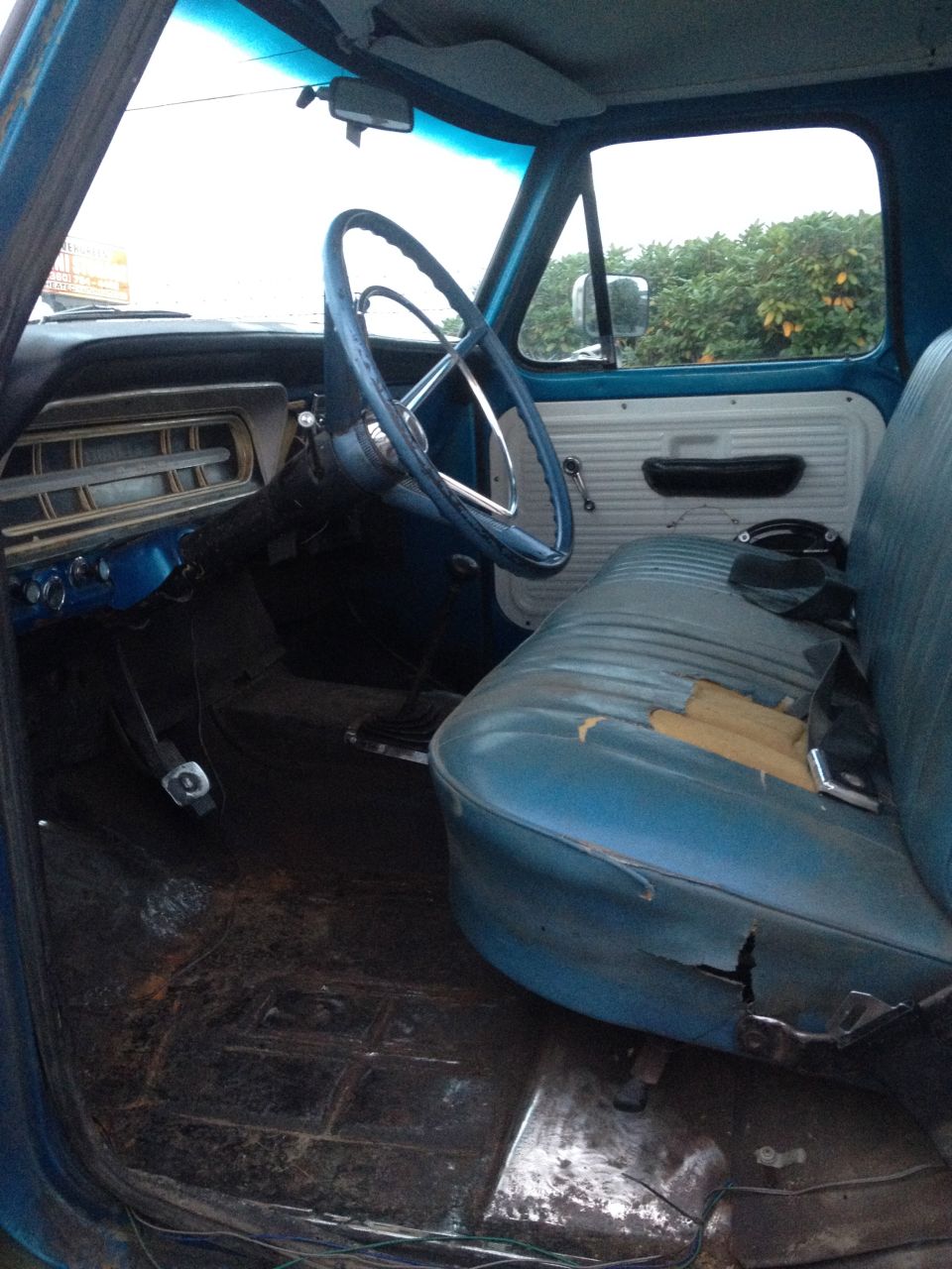 Interior of an old Ford truck with blue bench seat and two-tone metal door