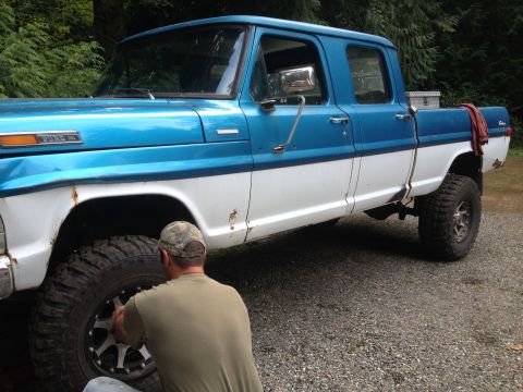 1971 Ford F-250 - A man works on the front wheel of a two-tone blue and white Ford F-Series truck.