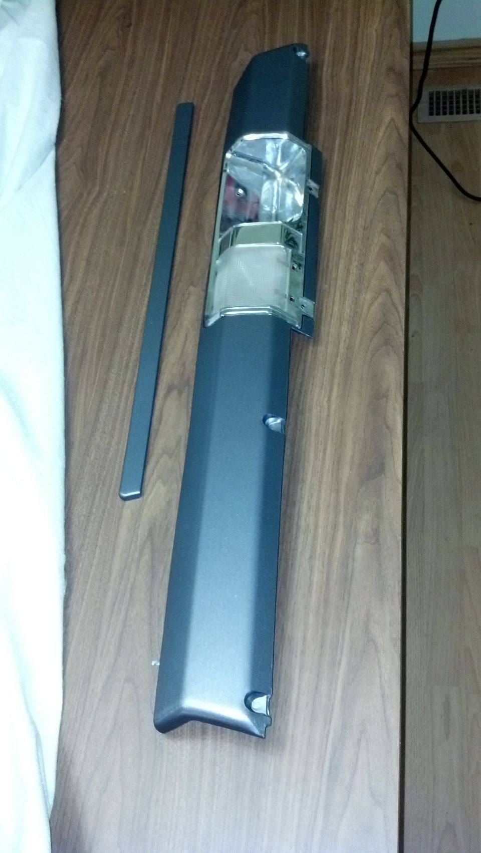 Dark gray car trim piece with chrome and clear plastic lens