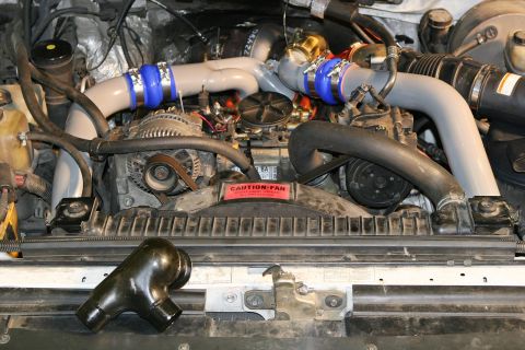 1988 Ford Bronco - Close-up of an engine bay, focusing on the turbocharger and associated piping. A caution fan sticker is visible.