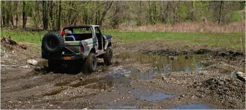 1979 Ford Bronco - Ford Bronco navigates a muddy off-road trail with trees and grass in the background.