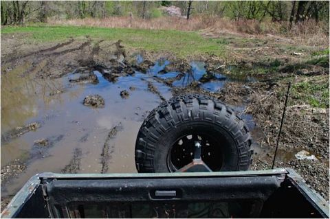 1979 Ford Bronco - Off-roading through a muddy field with a spare tire visible.