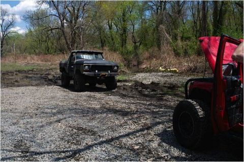 1979 Ford Bronco - A black pickup truck navigates a muddy terrain, with a red jeep partially visible in the foreground.