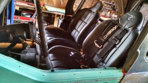 1985 Jeep CJ7 - The interior of a teal vehicle shows black racing seats with Corbeau harnesses and a roll cage.