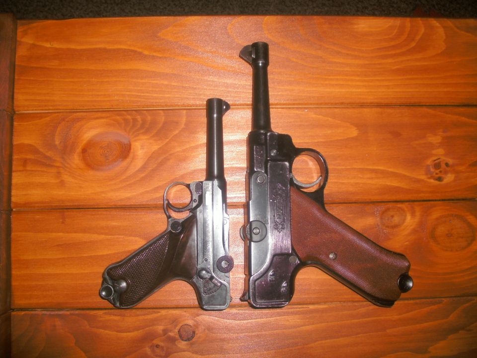 Two Luger pistols on a wooden surface. One is shorter than the other