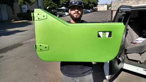 1985 Jeep CJ7 - A man holds up a bright green Jeep door, with the interior of a vehicle visible in the background.