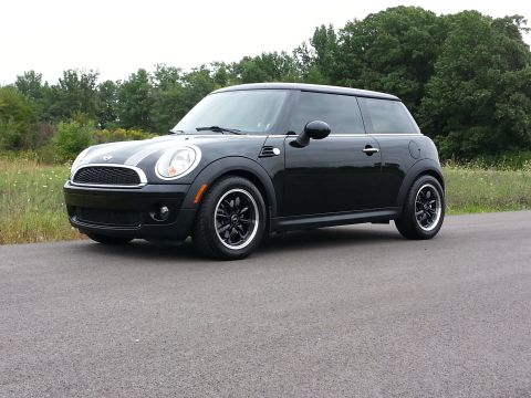 2010 MINI Cooper - A black MINI Cooper is parked on a road with trees in the background.